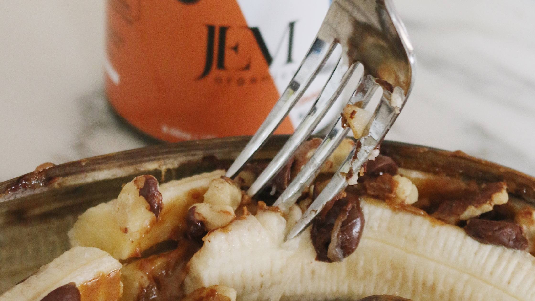 Fork digging into a stuffed banana with chocolate chips, nut butter and walnuts