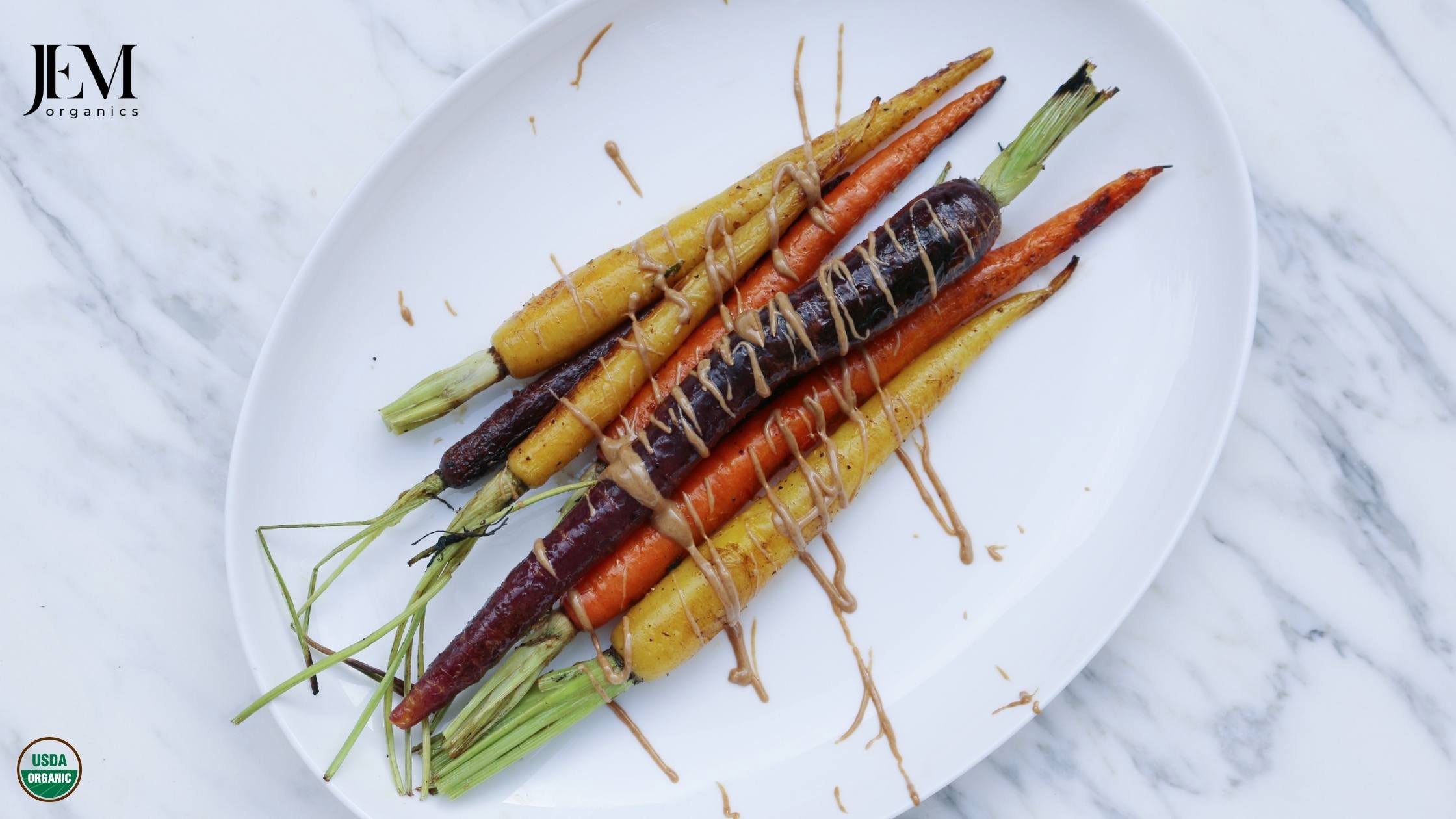 Roasted carrots on a white plate drizzled with JEM Organics almond butter