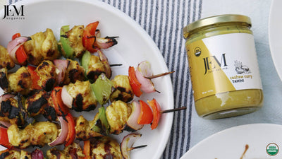 Chicken kabob with peppers and onions on a white plate next to a large jar of JEM Organics Curry Cashew Tahini