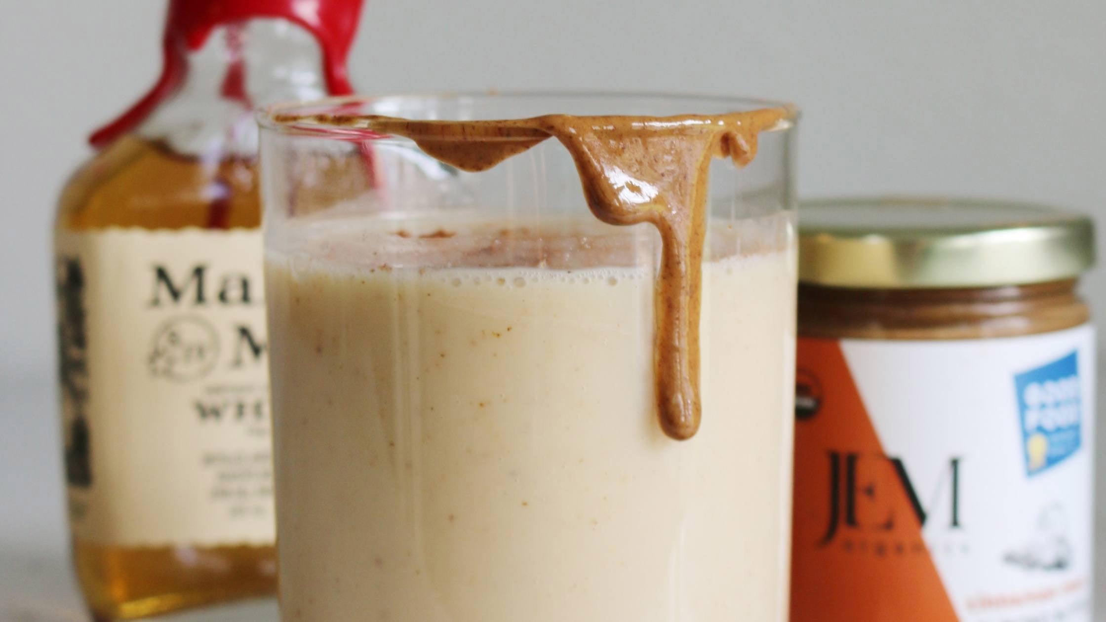 Glass of eggnog with JEM Organics nut butter jar and a bottle of Maker's Mark whiskey