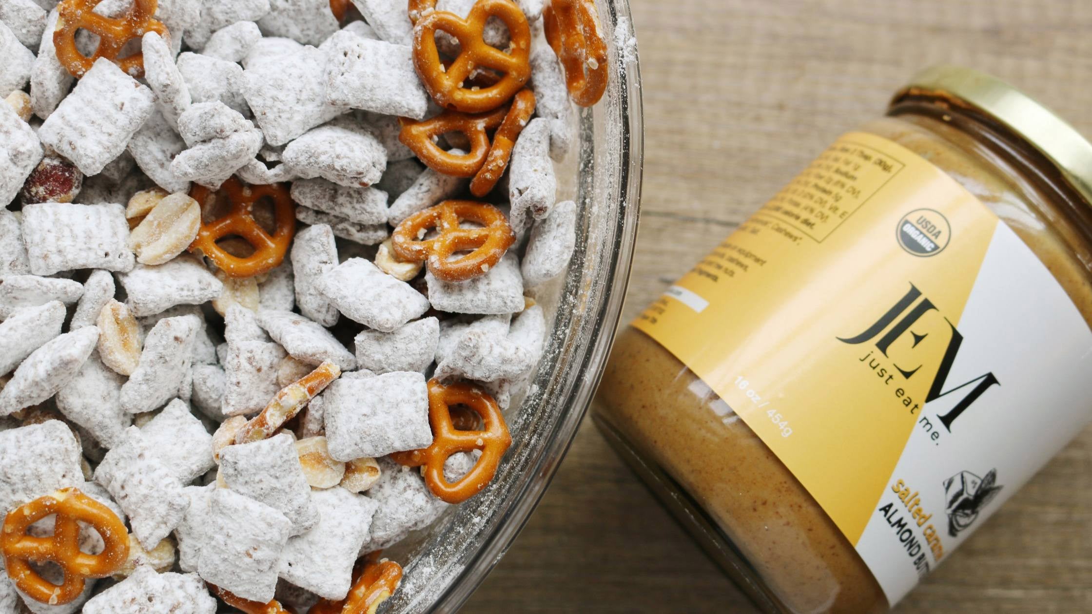 chex covered in powdered sugar and pretzels in a glass bowl next to a JEM Organics nut butter jar